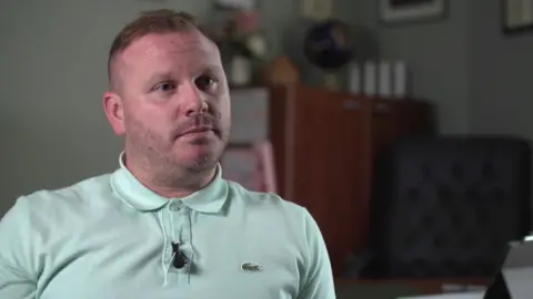 Portrait of Ciaran Mulholland in his office being interviewed by the BBC