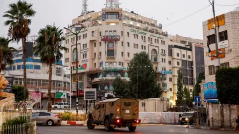 Reuters An Israeli military vehicle moves in a street outside the building in Ramallah, in the Israeli-occupied West Bank, where Al Jazeera's office was located before it was ordered to close (22 September 2024)