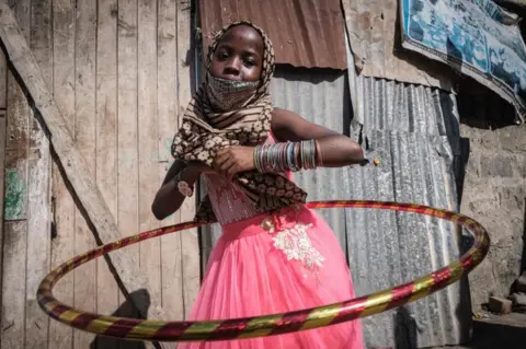 AFP A girl in a pink dress smiles as she plays with a shiny hula hoop.