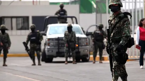 Getty Images Armed police in helmets and camouflage suits stand in front of a vehicle on the street