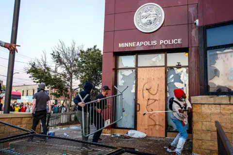 Getty Images Protesters use a barricade to try and break the windows of the 3rd Police Precinct