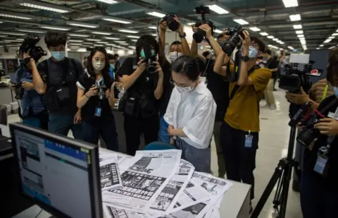 EPA A proof reader surrounded by members of the media works in the newsroom of the Apple Daily newspaper on 17 June 2021