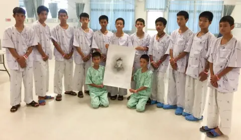 Reuters The 12-member "Wild Boars" soccer team and their coach rescued from a flooded cave pose with a drawing picture of Samarn Gunan, a former Thai navy diver who died working to rescue them, at Chiang Rai Prachanukroh Hospital