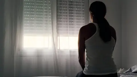 Getty Images Anonymous woman sitting on a bed looking out the window