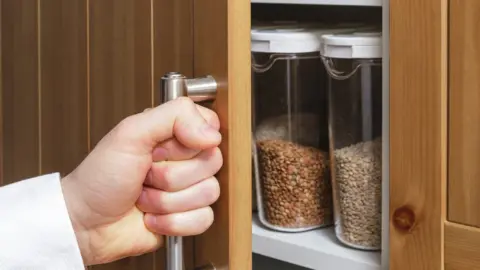 Getty Images Opening a kitchen cupboard containing storage jars