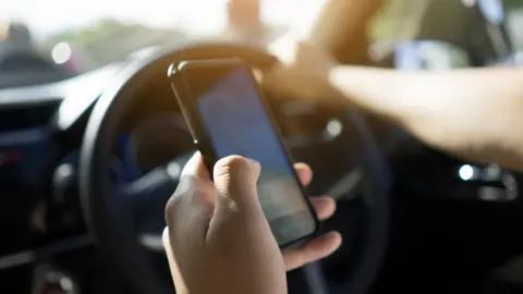 Getty Images A man uses a mobile phone in his hand to navigate while driving