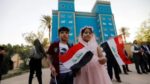 Reuters Children hold Iraqi flags during celebrations after Unesco designated Babylon as a World Heritage Site, in front of a replica of Ishtar gate near Hilla, Iraq, July 5, 2019.