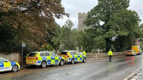 Edd Smith/BBC Five police vehicles and two police officers outside of St Martin's church in Overstrand.