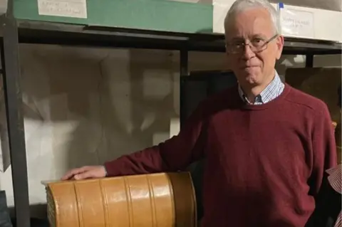 Durham University Prof Francis Watson is stood with his arm resting on the original codex. He is wearing a red sweated on top of a shirt.