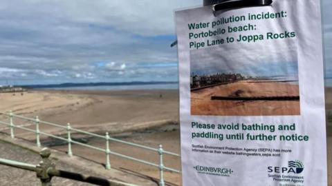 Laminated sign tapeed to a lampost, reading 'Water pollution incident: Portobello beach: Pipe Lane to Joppa Rocks. Please avoid bathing and paddling until futher notice' with Sepa and Edinburgh city council logo on bottom left and right. Portobello beach in the background with no people on the beach.