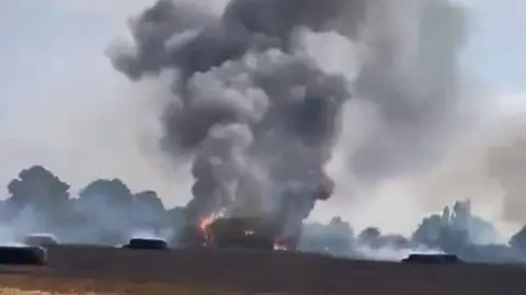 Craddock family A large plume of black smoke rising from a fire in a field.