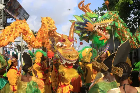 EPA/Shutterstock Carnival-goers dressed in matching outfits hold up a giant dragon puppet