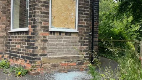 Simon Thake/BBC A window is boarded up with broken glass scatted on the ground below