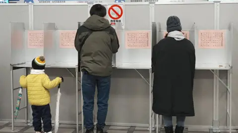 Getty Images A child (L) holds umbrellas as voters take part in the House of Representatives election at a polling station in Tokyo on February 8, 2026. 