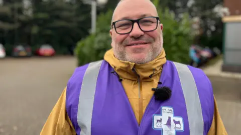 A male K9-SAR charity worker in a yellow coat and purple jacket. 