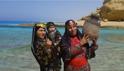 EPA A family wear traditional clothing and pose for a photo on the beach at Marsa Matruh in Egypt on 8 June.