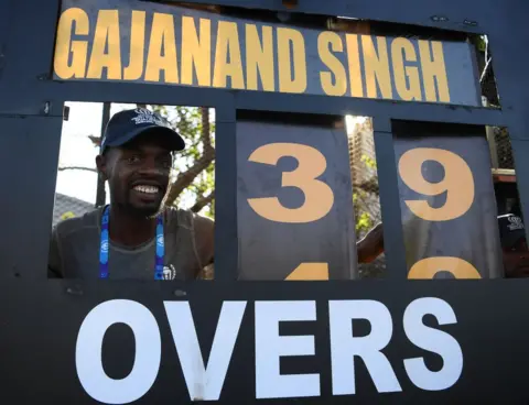Alex Davidson-ICC/Getty Images A scoreboard operator smiles through a gap in the board.