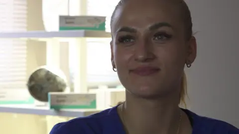 Zuzi Kam, a woman with ginger hair in a ponytail, sits inside a treatment room at So Me Beauty