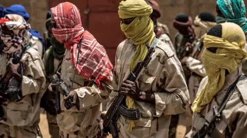 Getty Images A group of Fulani militiamen stand ready with their weapons at an informal demobilisation camp in Sevare - July 2019