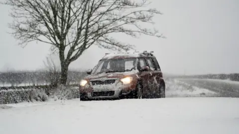 A car drives through snow on the A169 between Pickering and Whitby on the North York Moors