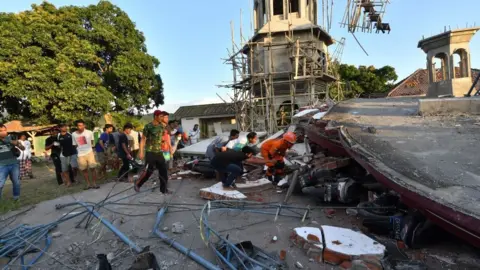 Getty Images Residents and Indonesian search and rescue personnel look under the ruins of a mosque in Pemenang