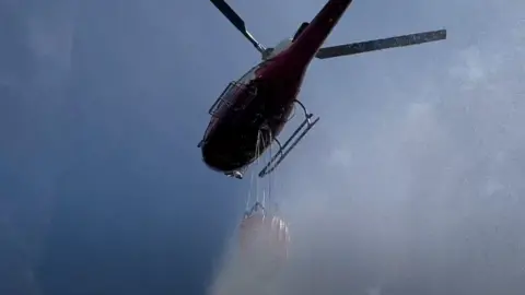 Helicopter spreading water over Surrey fires