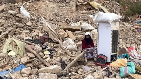 BBC A woman sits among rubble after a powerful earthquake struck the Moroccan village of Douzrou