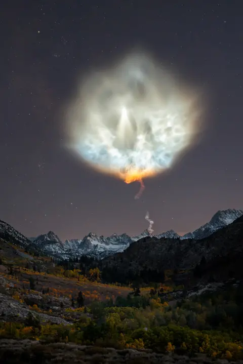 Nature TTL / Brandon Yoshizawa A landscape scene showing mountains at night with a large rocket exhaust plume in the sky