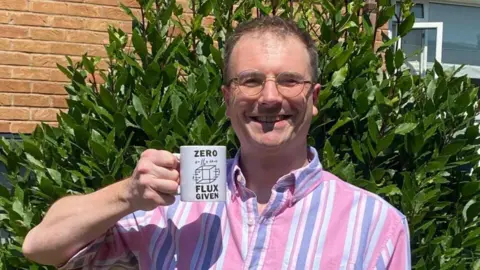 Tim Tim holding a mug that says 'zero flux given'