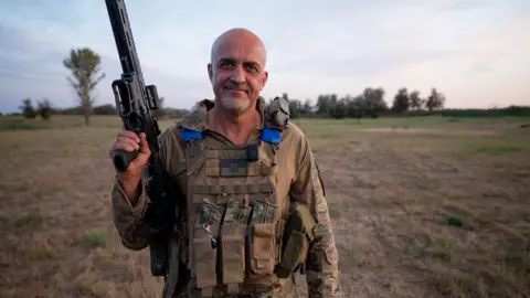 Lee Durant/BBC Ihor "The Knifer" stands with his gun aloft and a smile on his face in his uniform