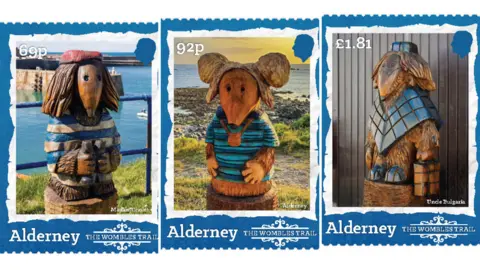 Three of the stamps. On the left is the 69p stamp which shows a Womble sculpture wearing a blue and white striped top and a red beret holding a pair of binoculars. It has shoulder-length hair and a pointed nose. Behind it is a bay. The middle stamp is a 92p one which shows a Womble sculpture wearing a multi-blue striped T-shirt and a bag around its neck standing in front of the sea. It has large round ears and a pointed nose. The one on the right is the £1.80 stamp. It shows a Womble wearing a diamond-patterned poncho and matching hat standing in front of a wooden panelled building. It has shoulder-length hair and is wearing a pair of glasses pushed down its pointed nose.
Each stamp features the silhouette of King Charles III's head and the wording: Alderney: The Wombles Trail.