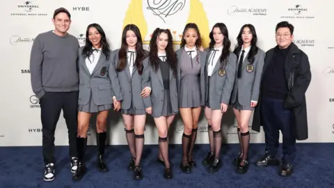 Getty Images (from left) John Janick (left), CEO of Interscope Geffen A&M Records, the six members of K-pop group Katseye, and Bang Si-Hyuk, Hybe chairman at a reality talent competition "The Debut: Dream Academy" 