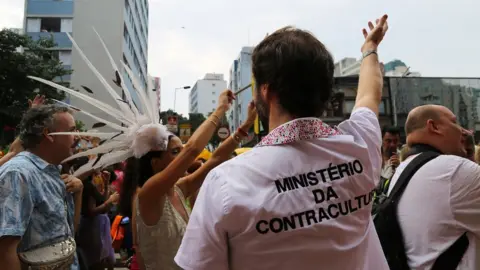 BBC A man wears a T-shirt emblazoned with a fake government department, the "Ministry of Counterculture"