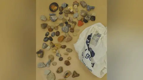 Suffolk Police Decorative stones and pebbles laid out on a table next to a white Boots carrier bag