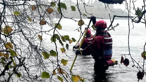 BBC Search and rescue workers wade through deep water as they look for a missing person