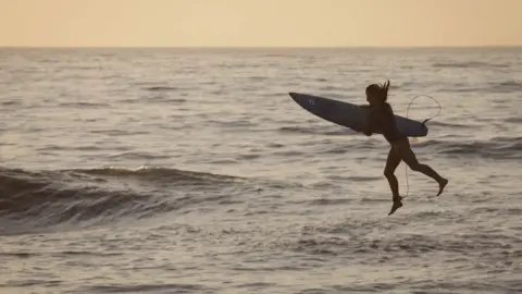 Kim Ludbrook/EPA A woman holding a surfboard jumps off a pier in Durban, South Africa - Sunday 28 May 2023