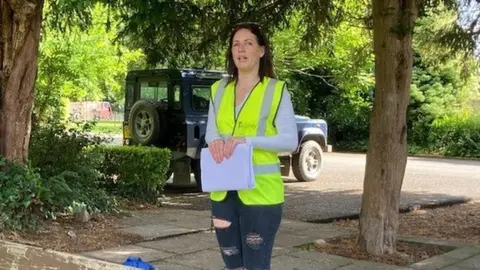 A woman standing on a pavement holding papers