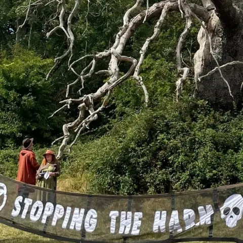 Indra Francesco  A banner reading Stopping the harm at the site of the oak tree