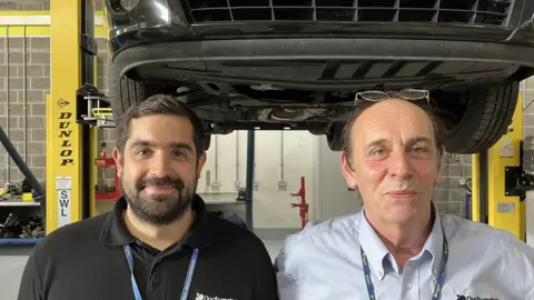 Ollie Conopo/BBC Man with dark hair and beard and man with short grey hair. Both wearing lanyards.