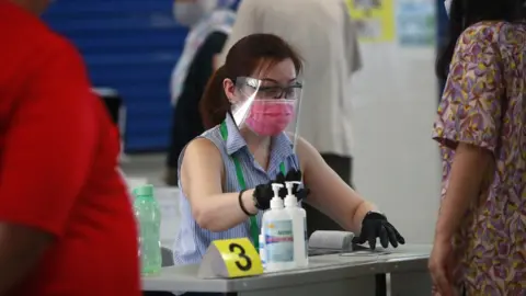 EPA An official checks a voter's papers at a polling station in Singapore, 10 July 2020