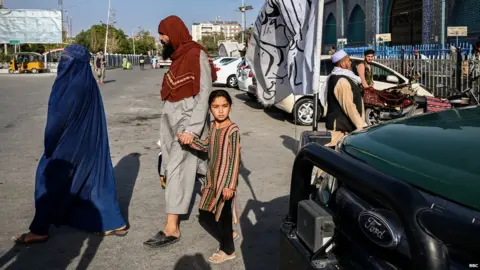 A girl passes by a car with the flag of the Taliban