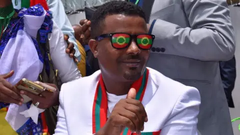 BBC Across the border in Ethiopia, one-time jailed politician Kefiyalew Tefera is dressed on Saturday in the colours of the Oromo Liberation Front to celebrate the return of the group's exiled leaders