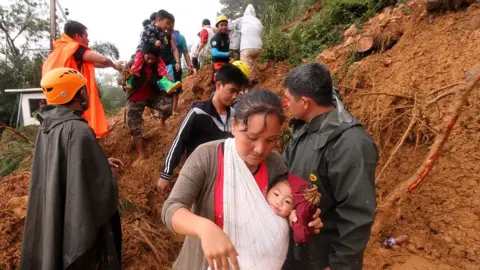 AFP People carrying children climb over muddy landslides in Itogon