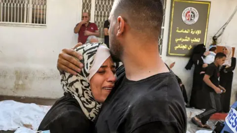 AFP via Getty Images A man comforts a woman mourning outside the morgue of al-Shifa hospital in Gaza City on October 12, 2023