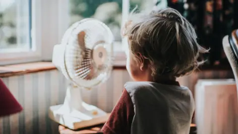 Getty Images A little boy stands in front of a fan