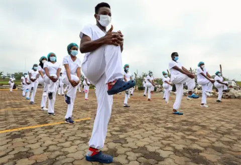 EPA Dozens of masked male and female health workers stand in formation as they stretch in sync.