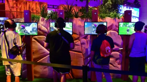 Getty Images Four gamers play Fortnite on a busy stand at the E3 2018 conference in LA