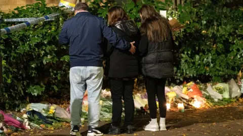 PA Media Leah Croucher's father John, mother Claire and sister Jade looking at flowers outside the house