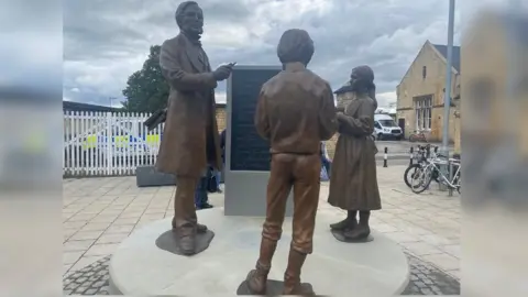 BBC The bronze artwork depicts a larger than life-size Boole teaching a boy and girl at a blackboard
