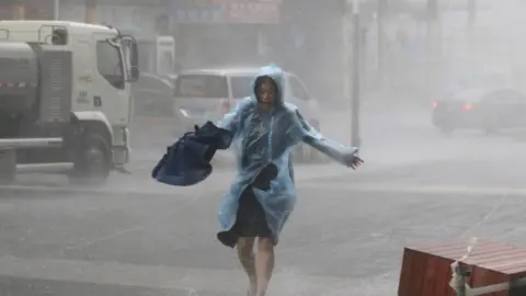 Reuters A woman runs in a waterproof with an umbrella in hand in heavy rainstorm in Shenzhen